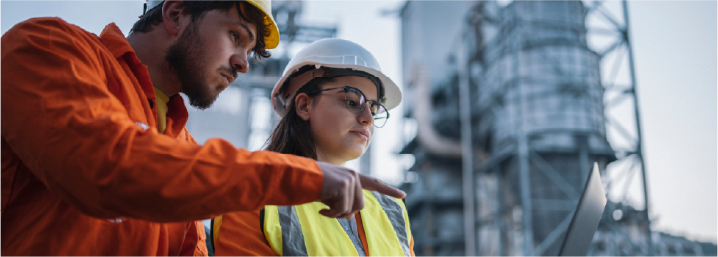 ingenieros revisando laptop con fábrica al fondo